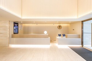 Uma área de recepção moderna com balcão de madeira, tela digital e bancada de atendimento.