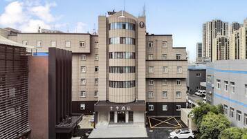 A hotel with a modern design, featuring a central entrance, multiple floors, and a parking area with cars.