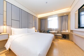 Quarto de hotel com uma cama grande, um sofá, uma mesinha, uma televisão e uma janela com cortinas.