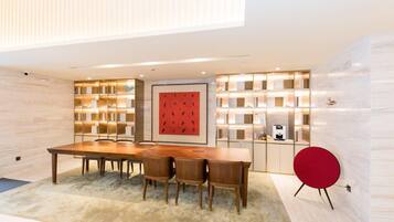 A modern dining area with a wooden table, chairs, a red accent chair, and a bookshelf with illuminated shelves.