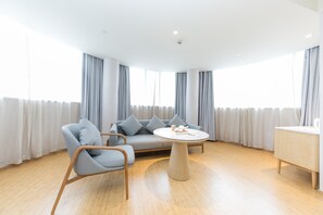 A modern living room with a sofa, two chairs, a round coffee table, and a wooden cabinet. - Ji Hotel Shanghai Shibei Hi-tech Park (Shanghai)