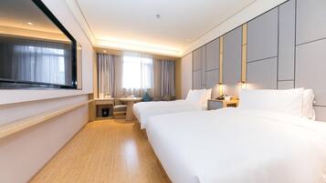 A hotel room with two beds, a TV, a desk, and a window with curtains.