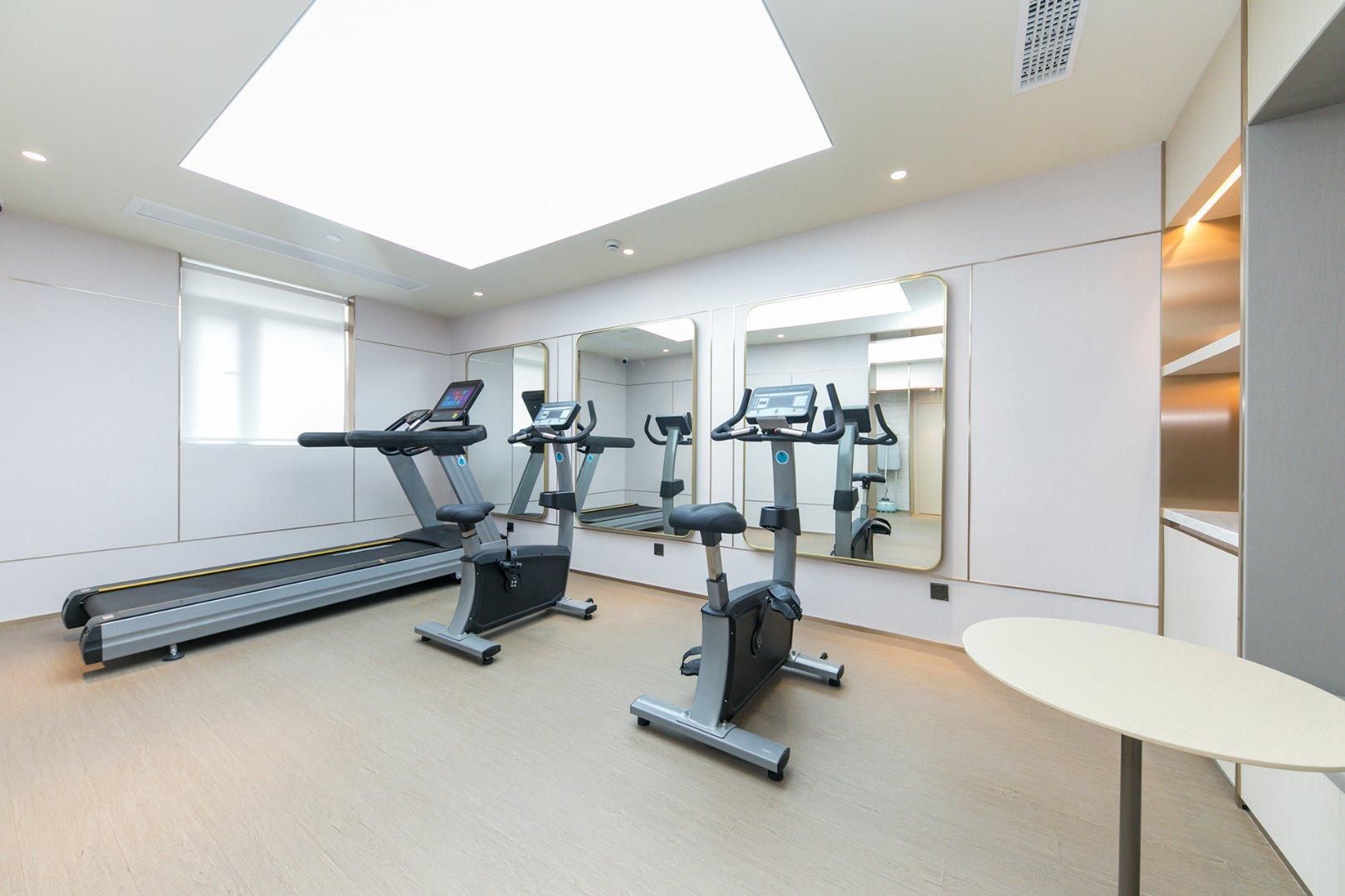 Ein modernes Fitnessstudio mit Laufbändern, Crosstrainern und einem großen Spiegel.