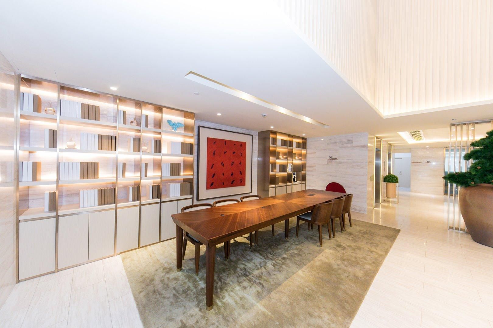 A modern dining area with a long wooden table, bookshelves, and a red abstract painting.