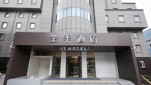 L’entrée d’un hôtel, avec une façade moderne, de grandes fenêtres et une enseigne indiquant « JI HOTEL ».