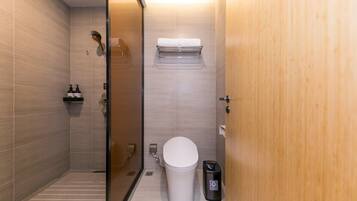 Un baño moderno con ducha de vidrio, inodoro, cubo de basura y toallero.