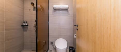 A modern bathroom with a glass-enclosed shower, a toilet, a trash bin, and a towel rack.