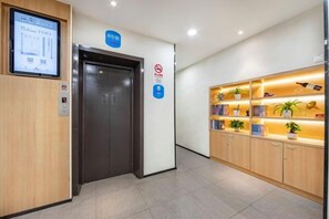 A hotel reception area with a reception desk, a digital display, a reception sign, a no smoking sign, and a plant shelf. - HanTing Hotel (Shanghai Xizang North Road Subway Station) (Shanghai)