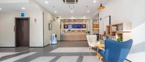 Een hotel lobby met een receptiebalie, een zithoek en een kitchenette op de achtergrond.