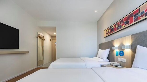 Ein Hotelzimmer mit zwei Betten, einem wandmontierten Flachbildfernseher, einem Nachttisch mit Lampe und einem großen abstrakten Gemälde über dem Bett.