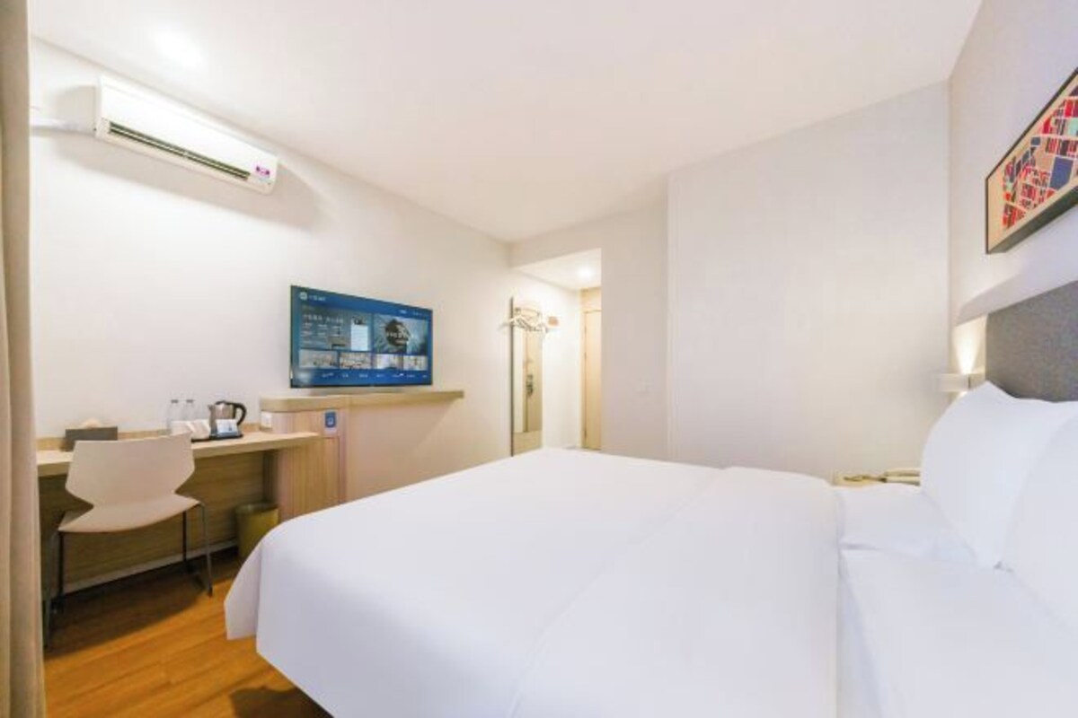 A hotel room with a bed, a desk with a chair, a television, and an air conditioning unit.