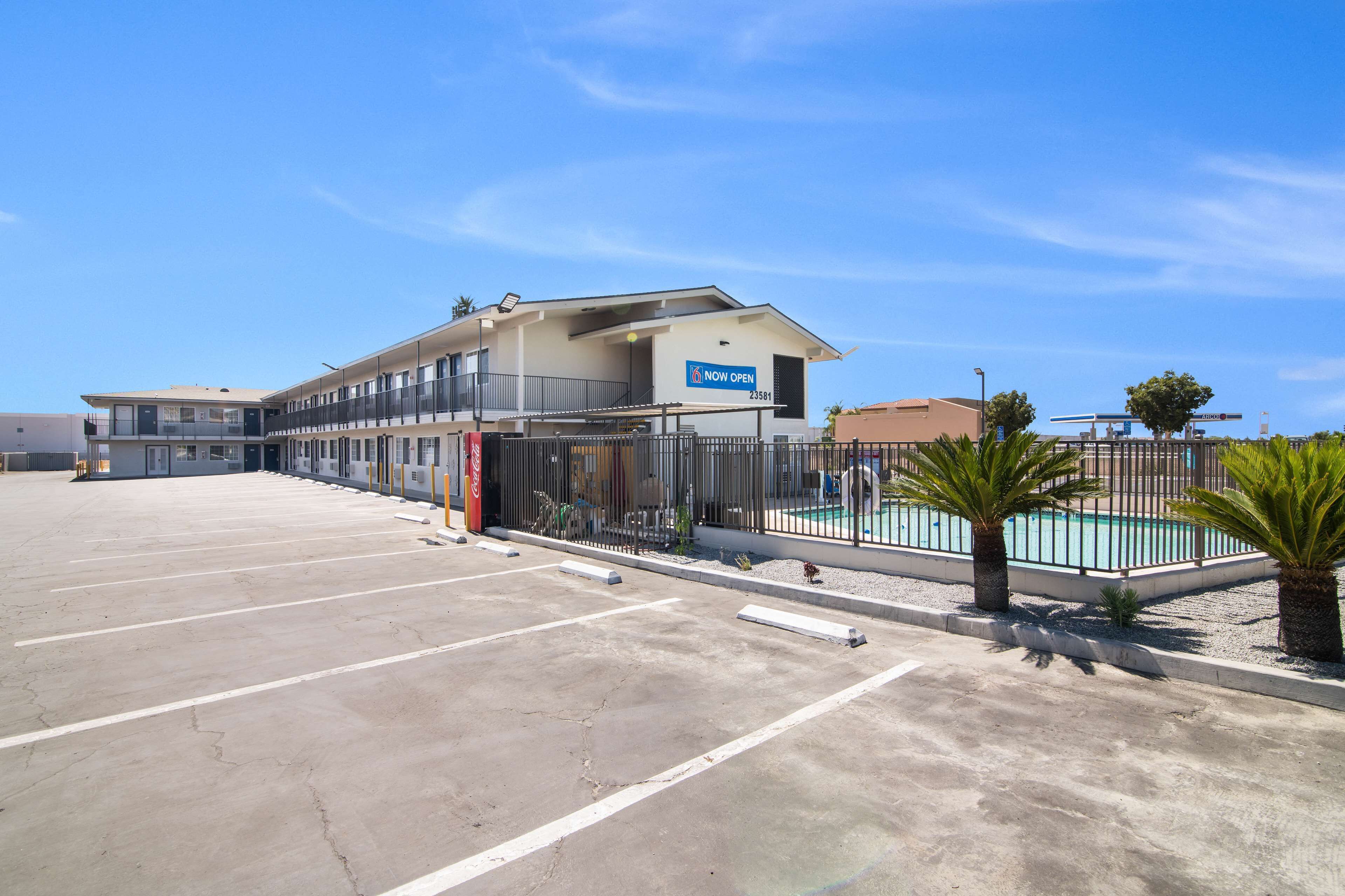 A hotel with a 'Now Open' sign, a swimming pool, and a parking lot.