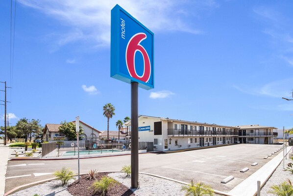 A motel sign with a number 6, a pool, and a building with multiple balconies.