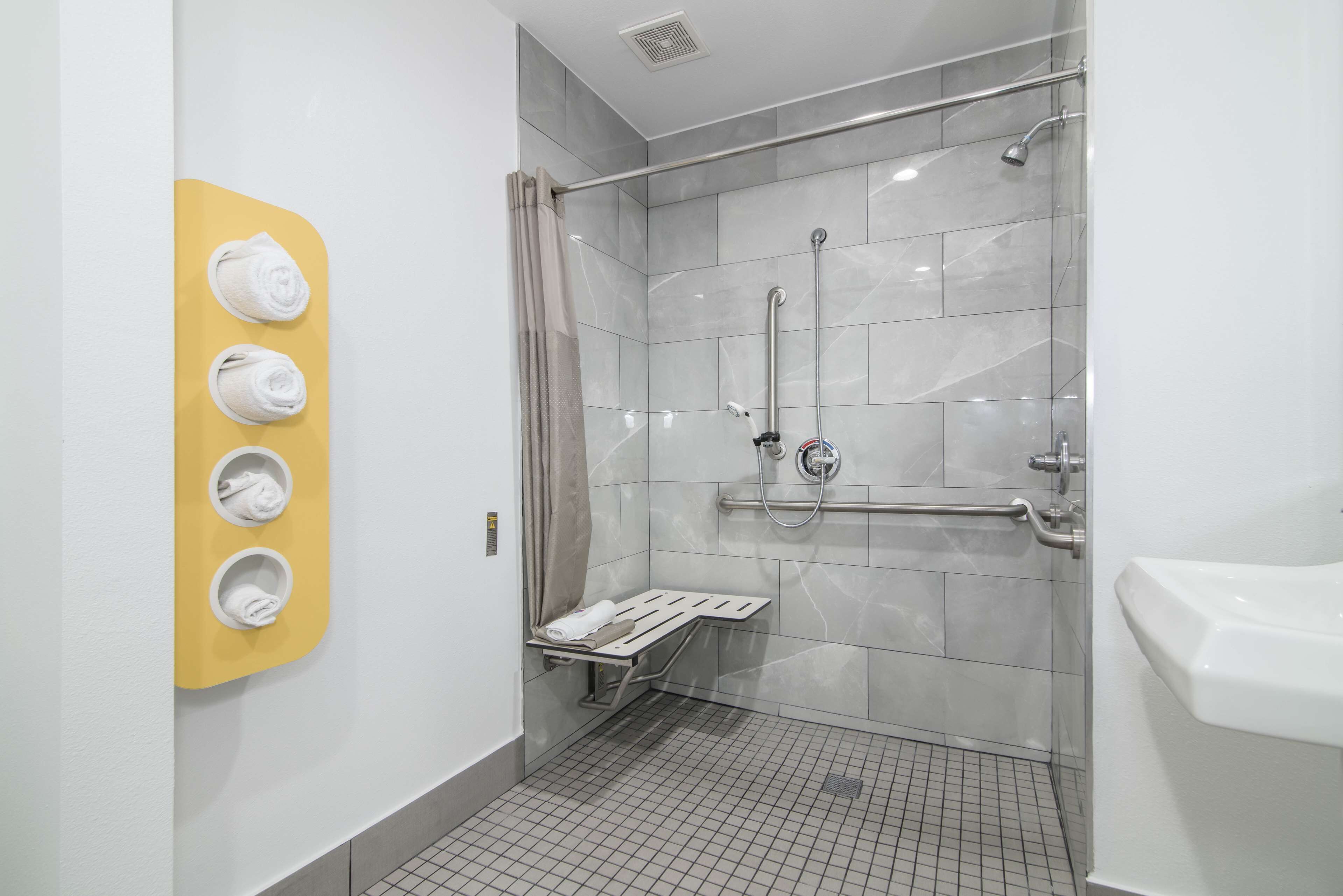 A modern bathroom with a glass-enclosed shower, a yellow towel rack, and a white sink.