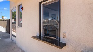 A building exterior with a large window, a door, and a small shelf. - Motel 6 Moreno Valley - Riverside March Air Base (Moreno Valley)