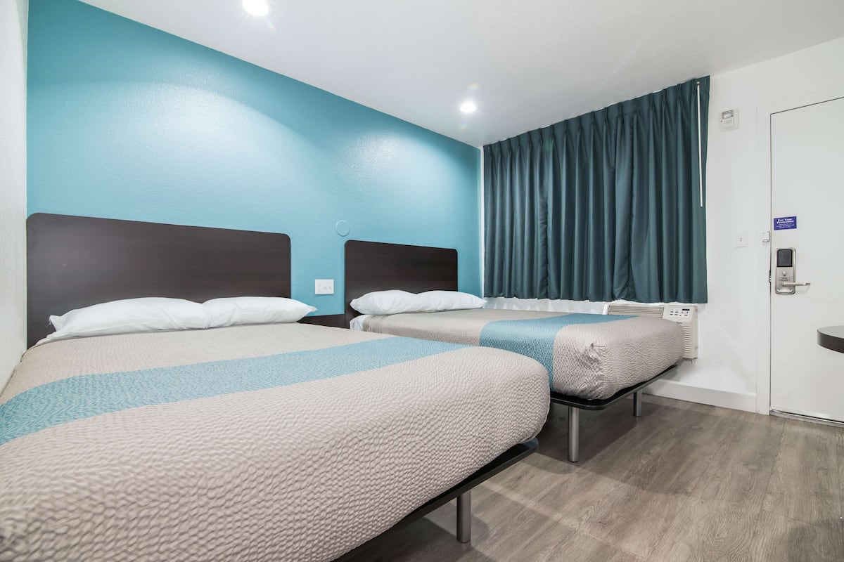 A hotel room with two beds, a blue accent wall, a dark blue curtain, and a white door.