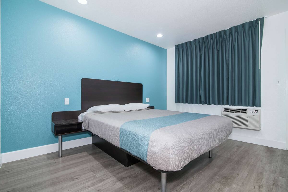 A modern hotel room with a bed, a nightstand, and a window with curtains.