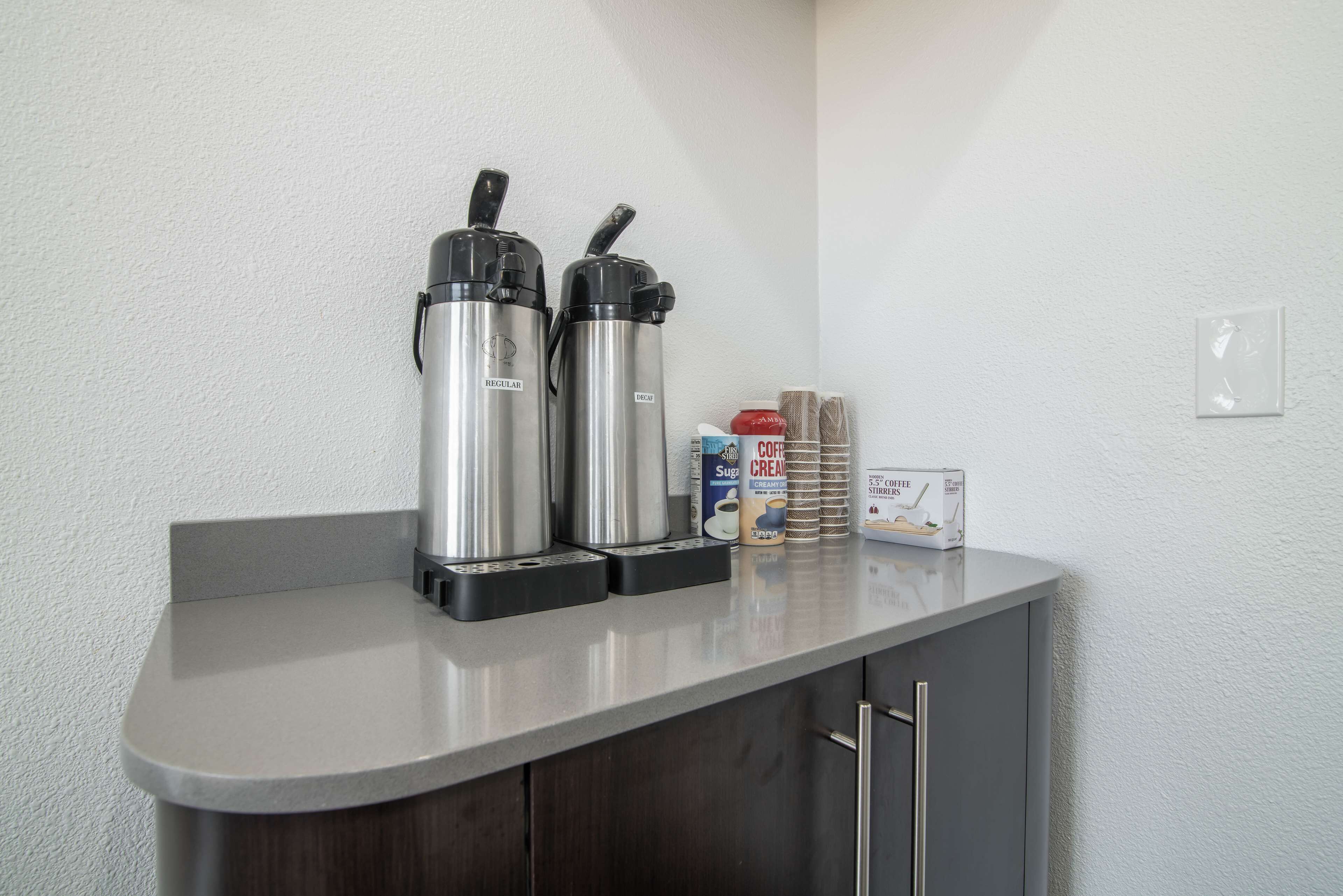 Une petite cuisine équipée de deux machines à café en acier inoxydable, d’un récipient à sucre et d’un distributeur de crème.