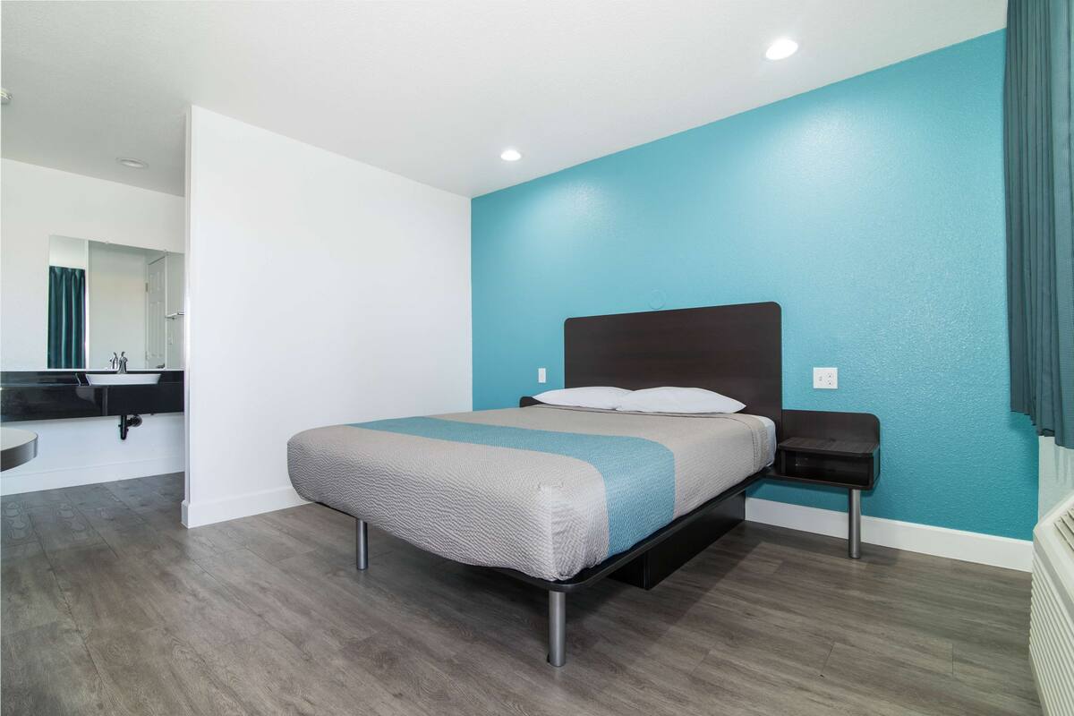 A modern bedroom with a bed, a nightstand, a bathroom with a sink, and a mirror.