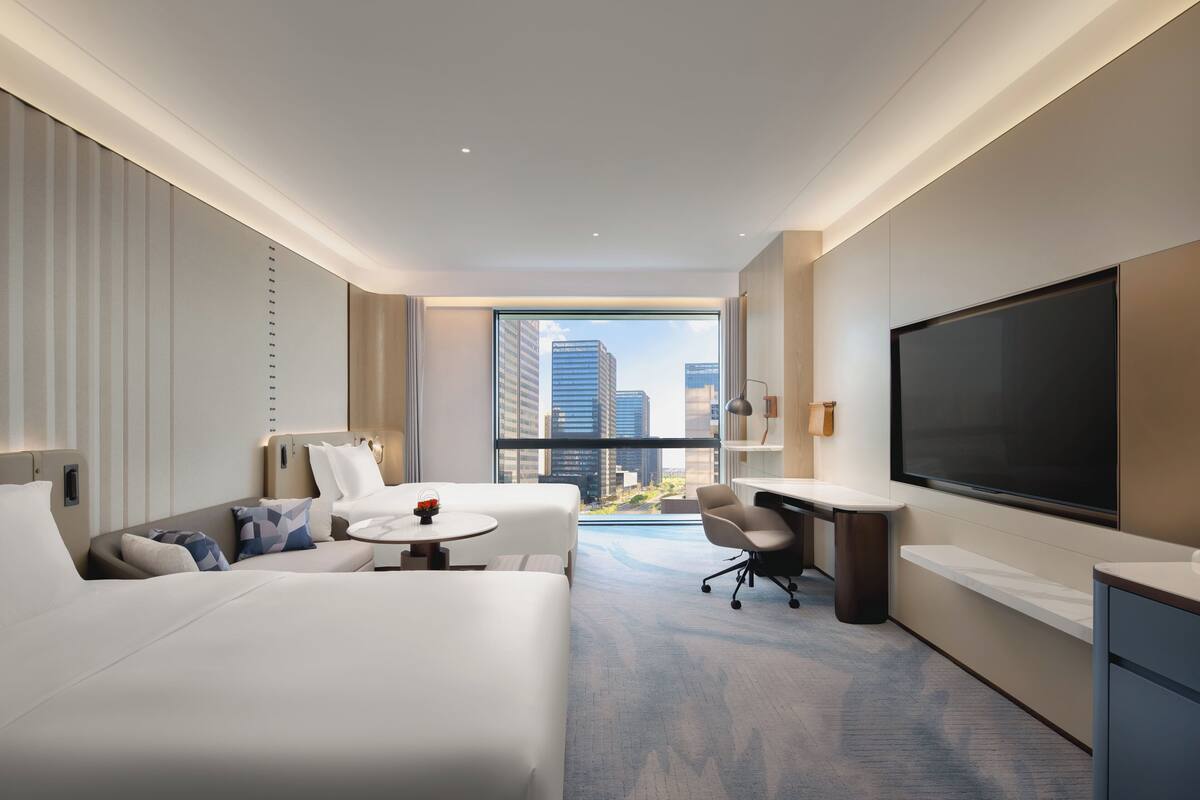 A modern hotel room with a large bed, a desk, a chair, and a TV.