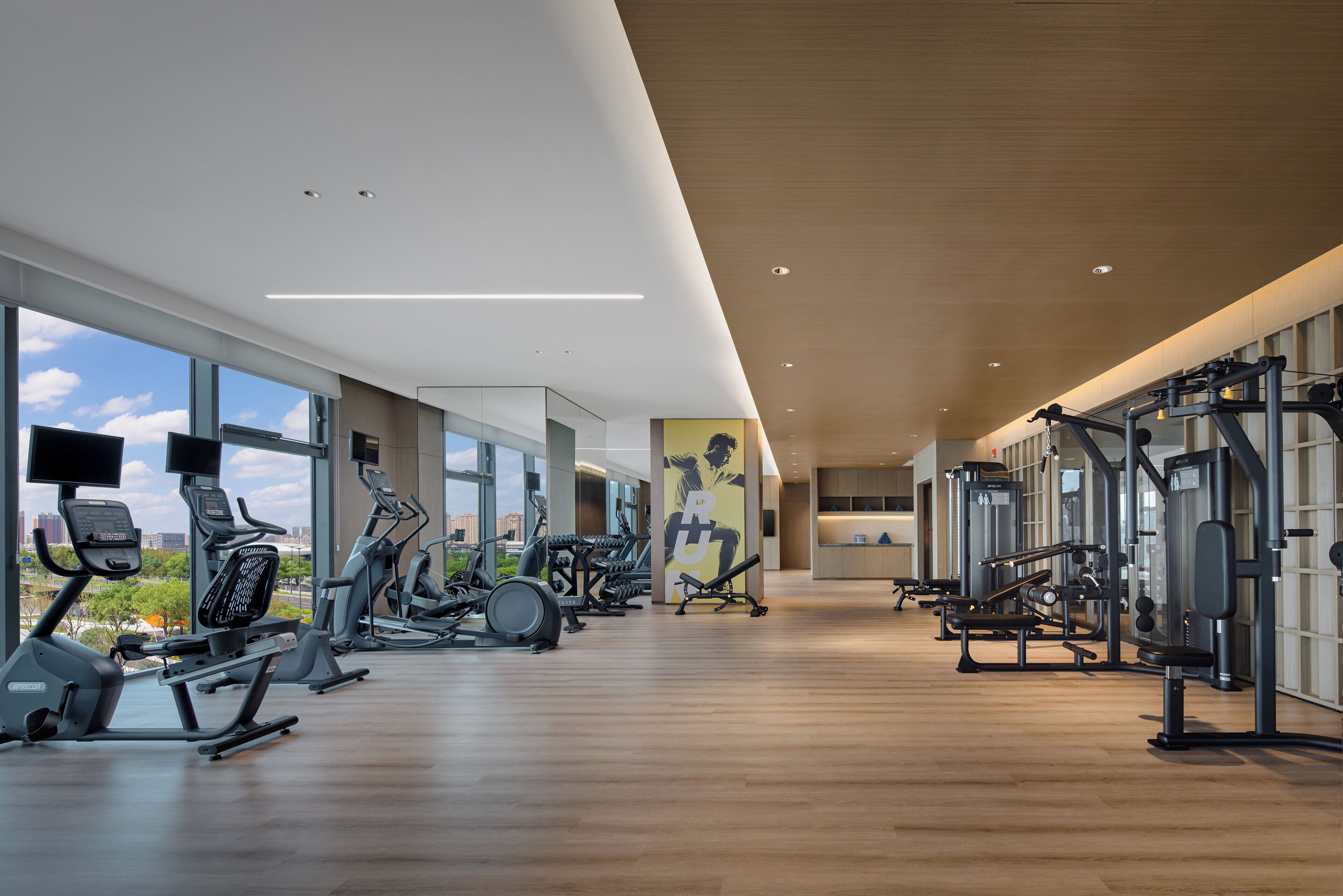 Ett rymligt gym med olika typer av träningsutrustning, stora fönster och en modern inredning.