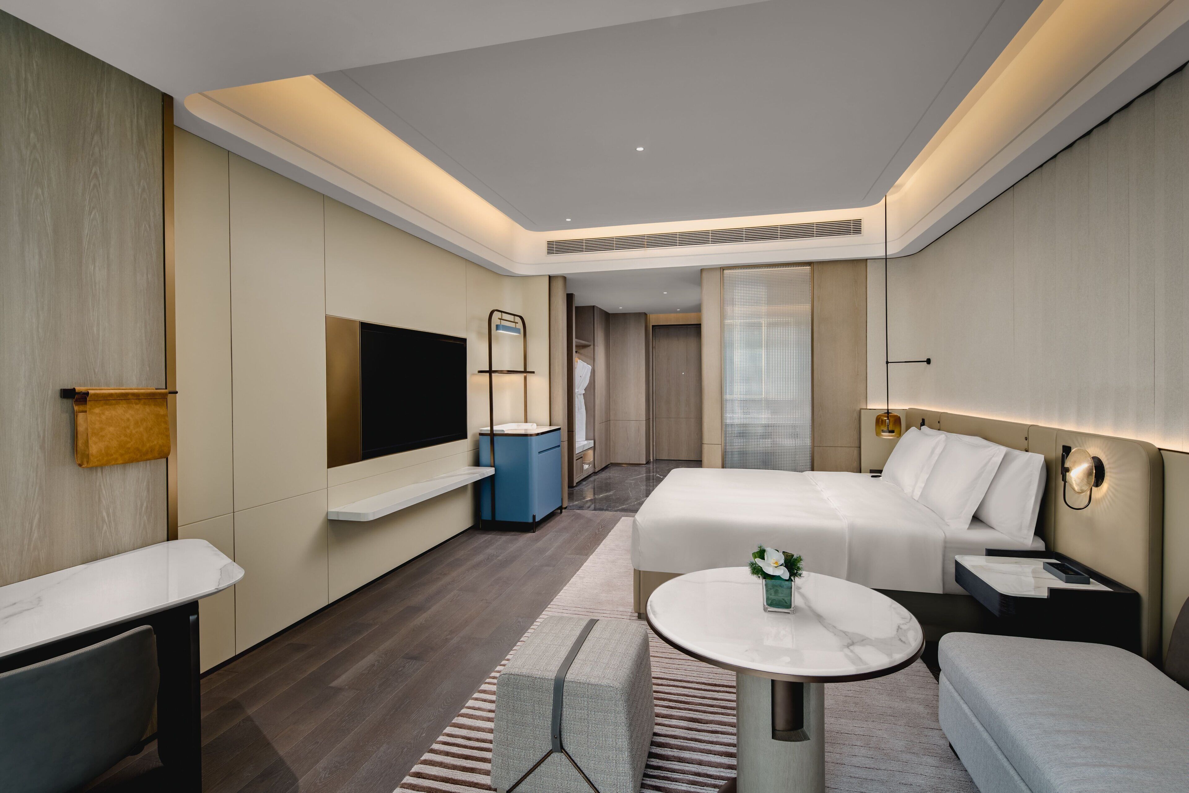A modern hotel room with a large bed, a TV, a small table, and a seating area.