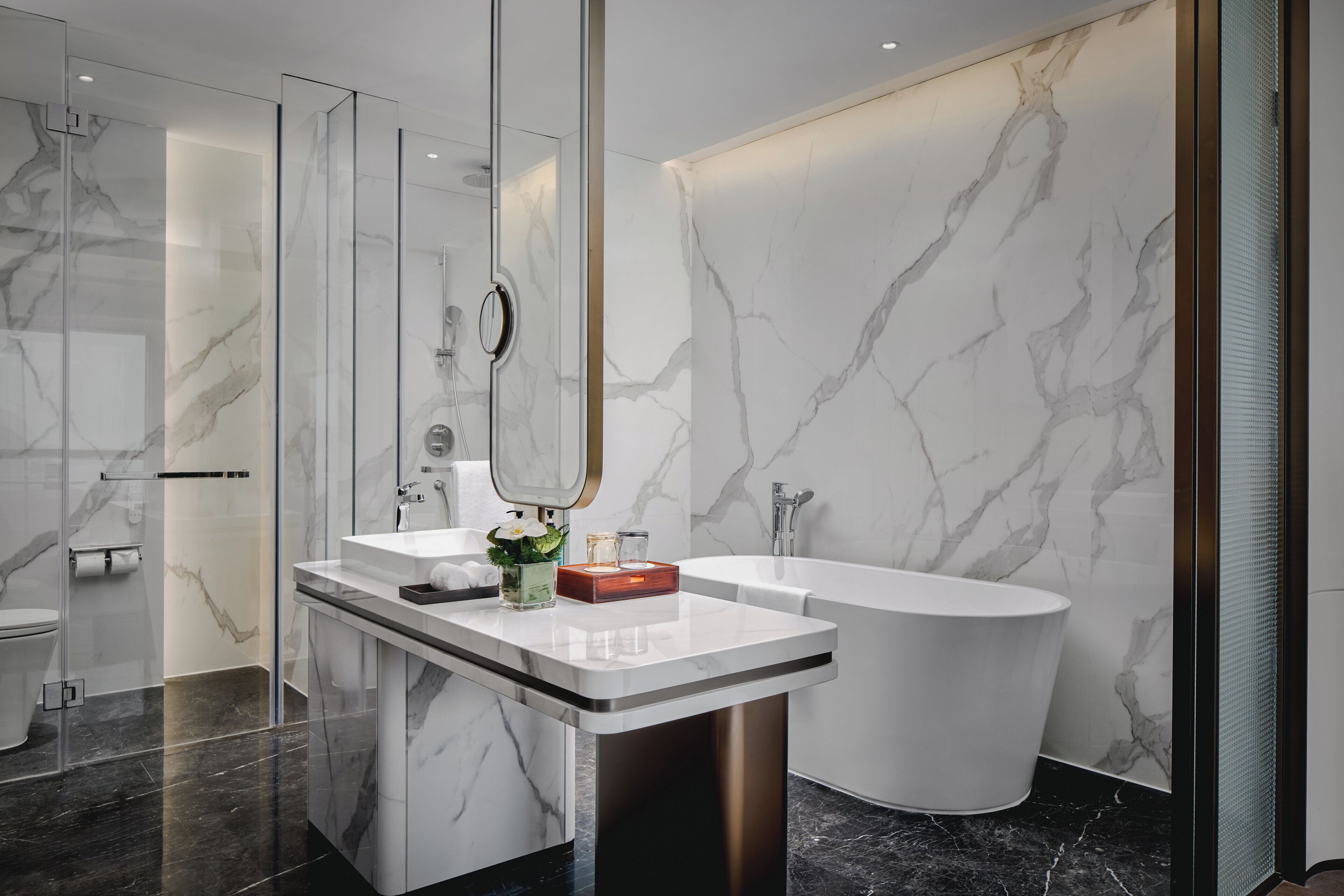 A modern bathroom with a glass-enclosed shower, a freestanding bathtub, and a vanity with a marble countertop.
