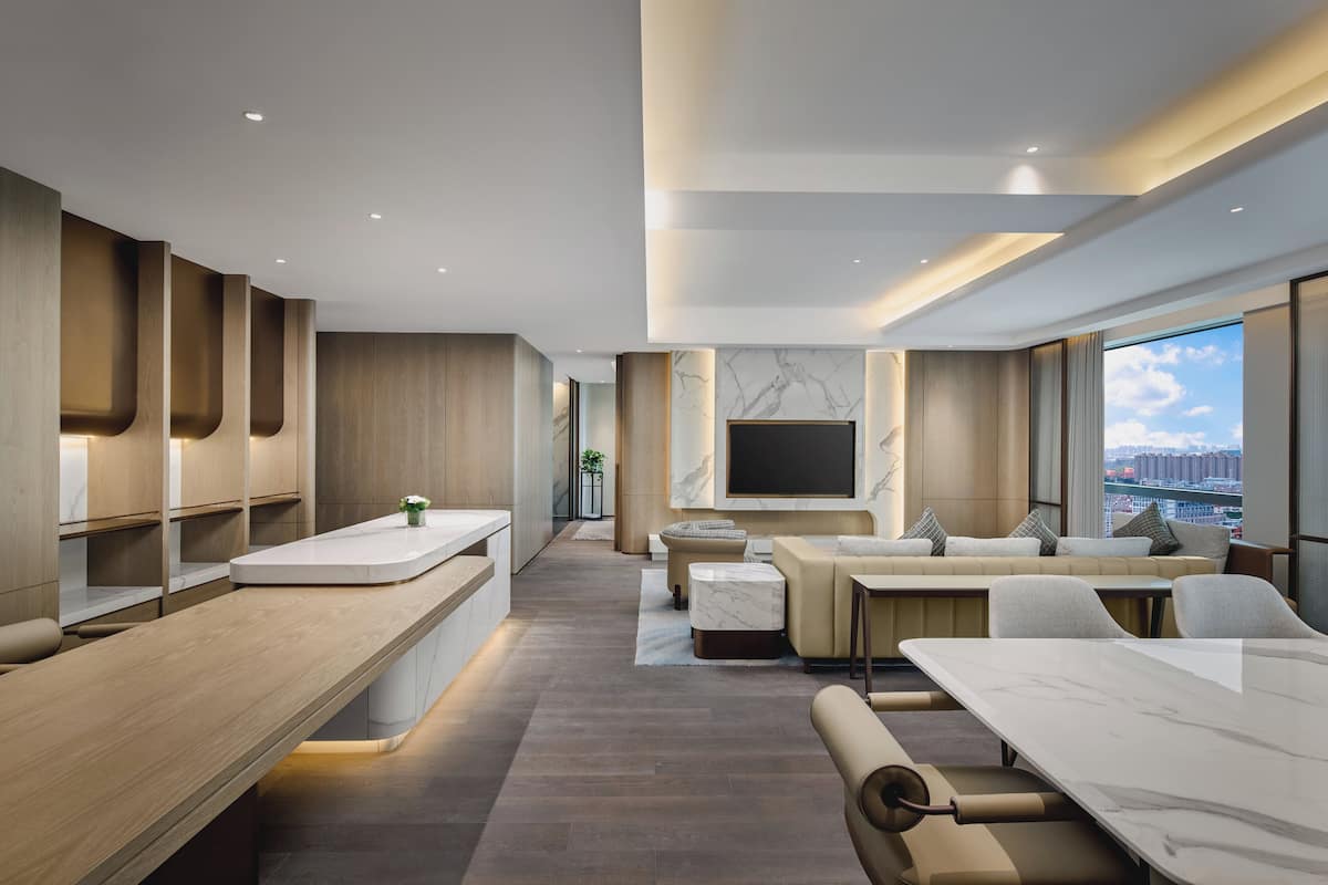 A modern hotel lobby with a long reception desk, seating area, and a large TV screen.