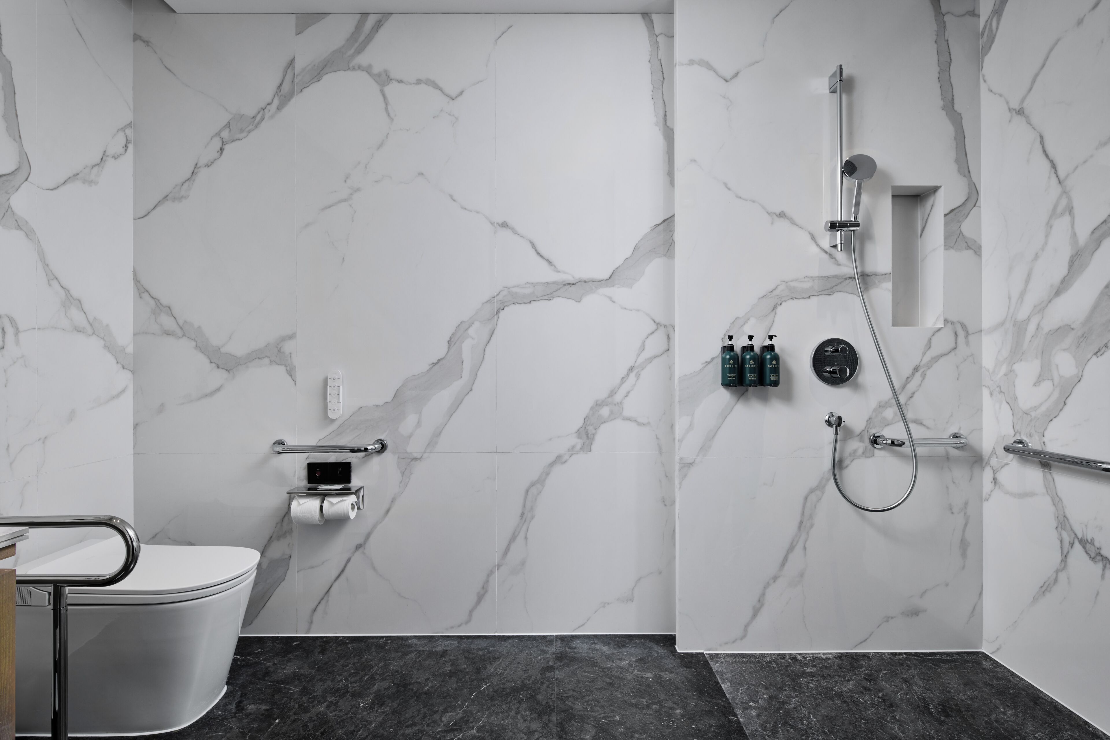 Ein modernes Badezimmer mit Marmorwand, Toilette, Dusche und Handläufer.