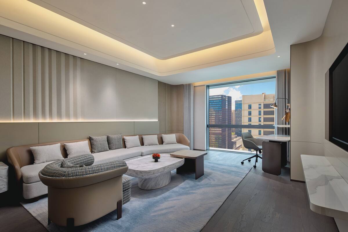 A modern living room with a sectional sofa, a round coffee table, and a large window offering a city view.