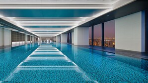 A long indoor swimming pool with a tiled floor and a view of a cityscape at dusk. - Crowne Plaza Kunshan East by IHG (Suzhou)