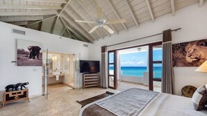 A spacious bedroom with a large bed, a TV, and a view of the ocean. - Villa Mumbai (Lowlands)