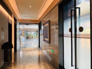 A hotel corridor with a polished marble floor, wooden paneling on the walls, and a glass door with a push button. - Ji Hotel(shanghai Meilong Wanhui International Pla (Shanghai)