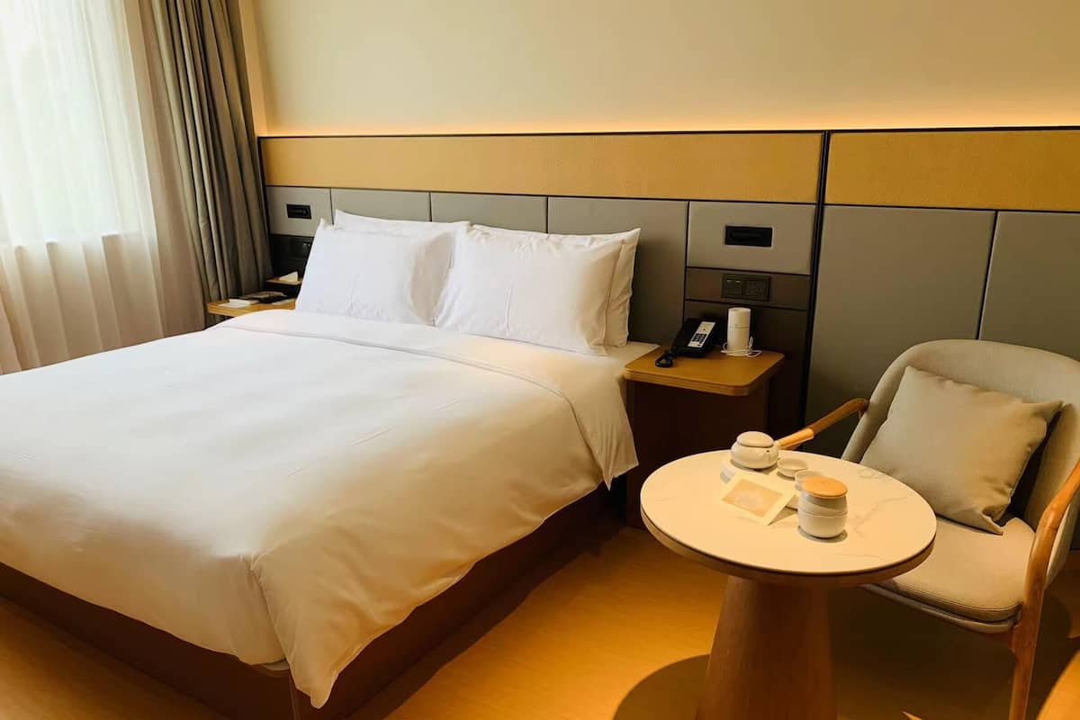 A hotel room with a large bed, bedside tables, a chair, and a small round table with a cup and a book.
