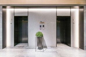 An elevator area with a potted plant, two elevator buttons, and a small shelf above the buttons. - Ji Hotel(shanghai Meilong Wanhui International Pla (Shanghai)
