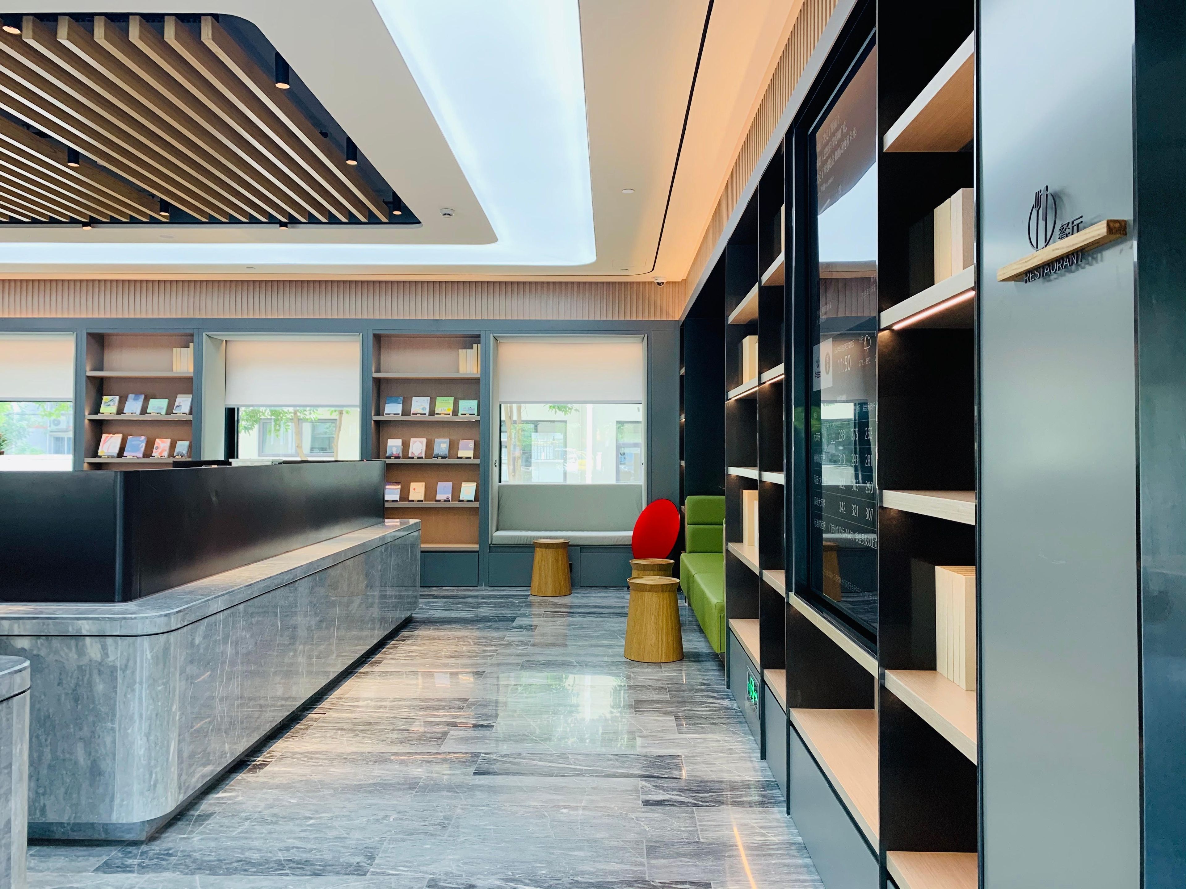 A modern interior with a reception desk, shelving with books, and a seating area with a red chair.