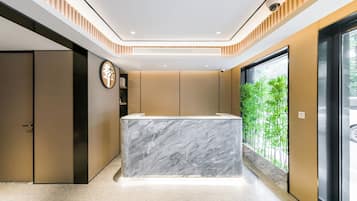 A modern reception area with a marble counter, a clock, and a view of greenery through a large window.