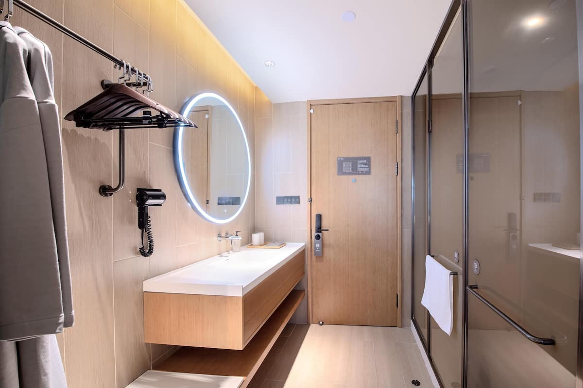 A modern bathroom with a wooden vanity, a mirror with a light, a towel rack, and a glass shower enclosure.