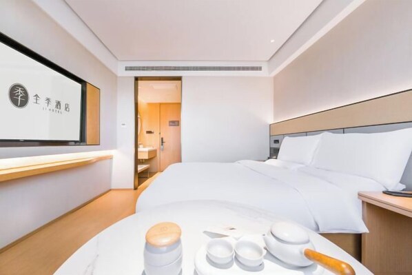 Una habitación de hotel moderna con una cama bien tendida, una mesita de noche y una pequeña mesa con un juego de té.