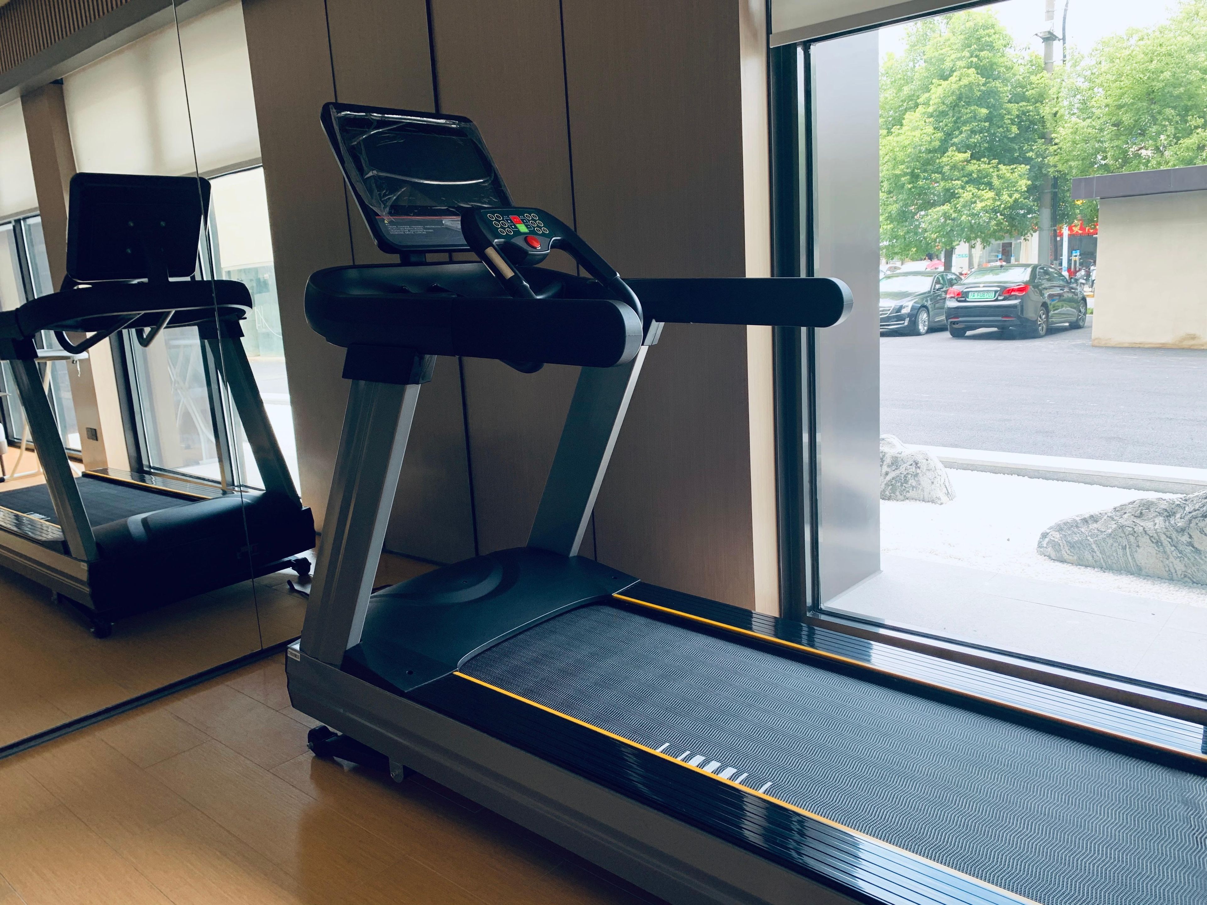 Un gimnasio con cintas de correr, una ventana que ofrece vista a la calle y piso de madera.