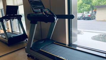 Un gimnasio con cintas de correr, una ventana que ofrece vista a la calle y piso de madera.