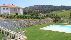 Une maison à deux étages, dotée d’une façade en pierre et d’un toit recouvert de tuiles rouges, entourée d’une pelouse bien entretenue et d’une piscine.