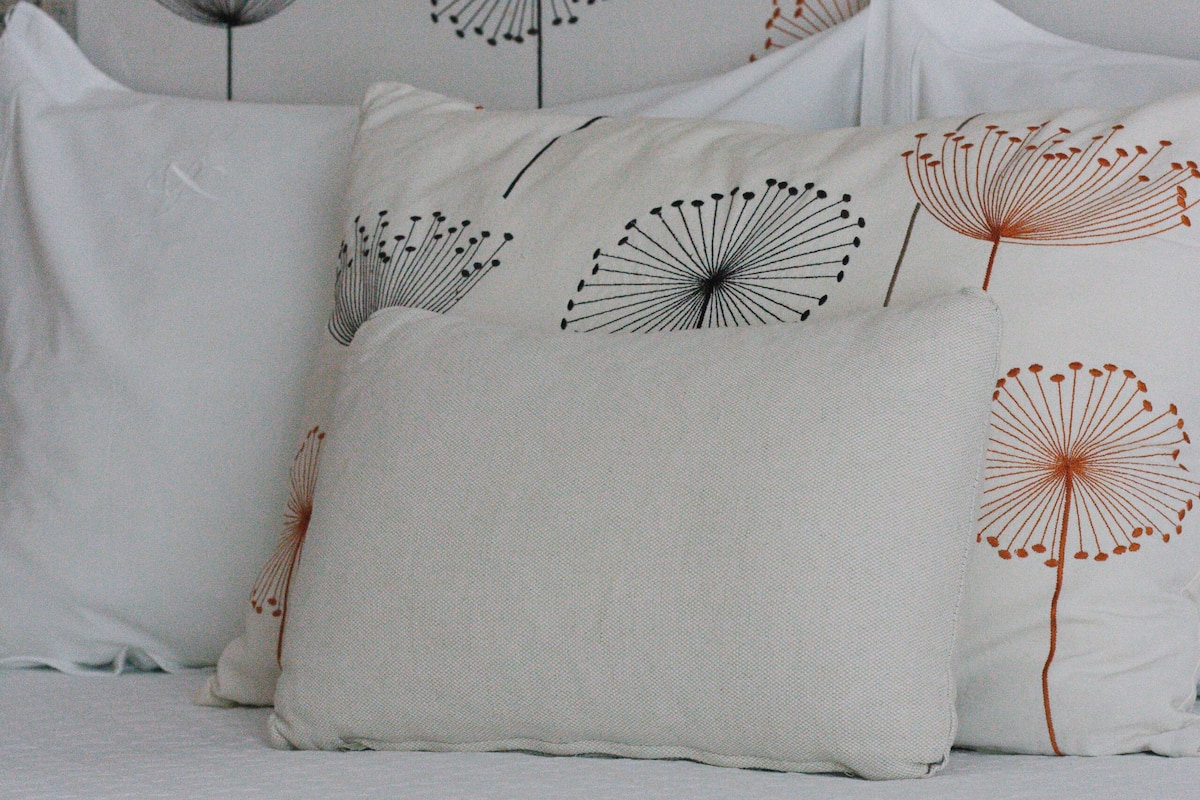 Una cama con ropa de cama y almohadas blancas decoradas con un diseño de diente de león.