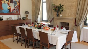 Une salle à manger avec une cheminée en pierre, des nappes blanches, des chaises en bois et un tableau accroché au mur.