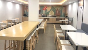 A dining area with multiple tables and chairs, a kitchen area with appliances, and a colorful mural on the wall. - Hanting Hotel Shanghai Macau Road (Shanghai)