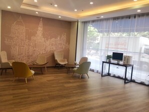 Un espace d’attente moderne agrémenté d’une fresque représentant un paysage urbain, de sièges confortables, d’un bureau avec un ordinateur et de grandes fenêtres.