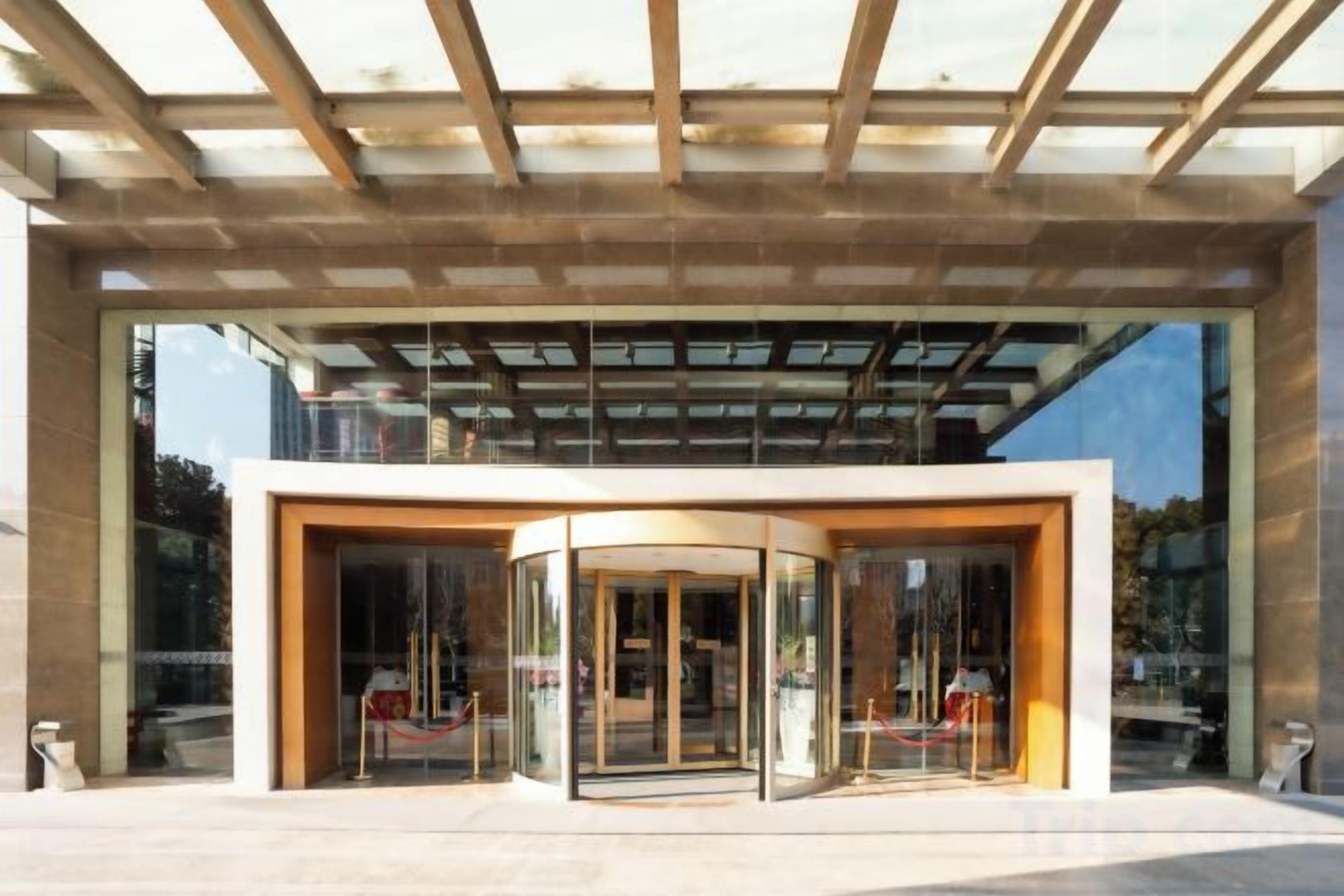 A modern building entrance with a glass facade, a curved glass door, and a wooden ceiling structure.