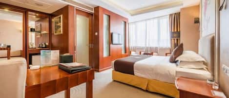 A hotel room with a bed, a desk, a chair, a TV, and a wardrobe.