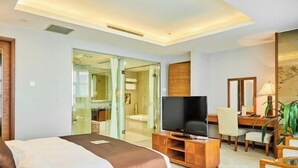 A hotel room with a bed, a television, a desk with a chair, and a mirror. - Chuzhou King House Hotel. (Chuzhou)