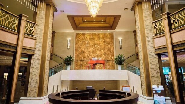 A lobby with a grand chandelier, a reception desk, and a patterned wall. - Chuzhou King House Hotel. (Chuzhou)